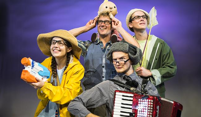 Four brightly dressed people, all wearing glasses, holding an array of objects: to the left, a smiley woman in a yellow raincoat and rain hat holds an