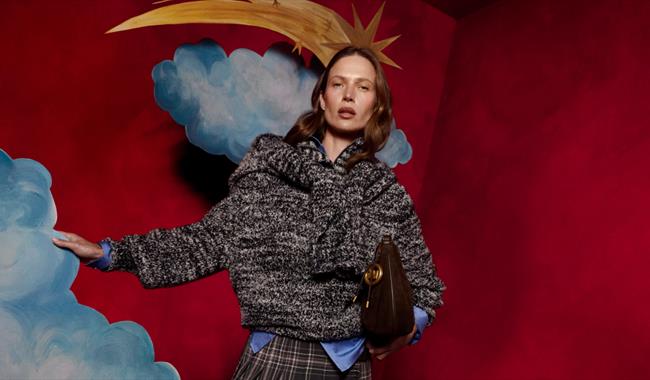 Woman in Winter clothing infront of a red background with large cardboard clouds and a gold shooting star