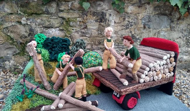 Knitted land girls from WW2 lifting logs.