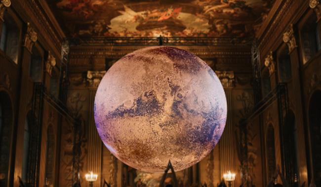 In a grand, ornate hall with a high, frescoed ceilings (the Painted Hall), a large, glowing model of planet Mars is suspended in the centre of the roo