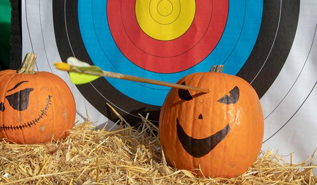 A pumpkin that has been shot by an arrow, in front of an archery target