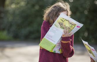 A young girl in a pink jumper writing on an Easter Trail sheet in the garden