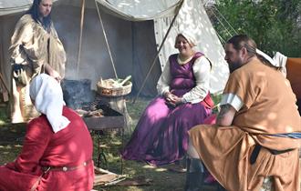People dressed in medieval clothes sat around an open fire