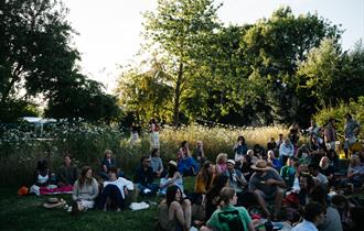 people sitting in the grass all together on picnic mats and chairs