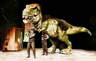 A huge green Tyrannosaurus Rex puppet operated by two puppeteers.