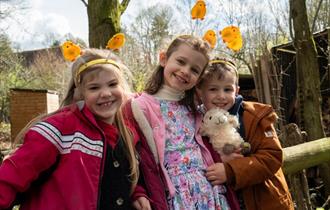 Three smiling children with Easter chick headbands at Chiltern Open Air Museum. One of the children is holding a cuddly sheep toy.