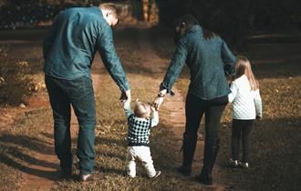 Young family walking a green forest and holding hands with their toddler