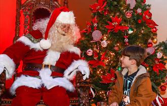 Father Christmas and a child with a Christmas tree in the background.