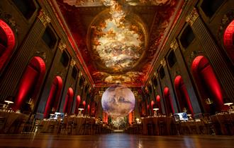 In a grand, ornate hall with a high, frescoed ceilings (the Painted Hall), a large, glowing model of planet Mars is suspended in the centre of the roo