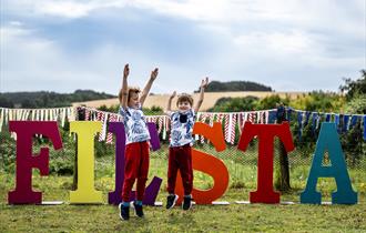 Two boys jumping in the air in front of big letters that spell 'Fiesta'