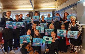 Painting party group holding finished paintings on canvases of Highland cows
