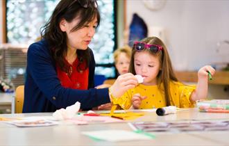 Adult and Child sitting at a table with art supplies. Adult is helping child with creating.