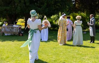 Visitors in Regency dress walking across the cottage garden at Jane Austen's House in summer