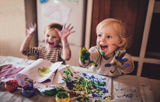 Two children being creative with paint and smiling at the camera