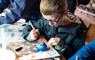 Boy in coat drawing a face on a sand filled balloon.