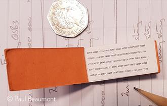 A small code book used for number stations, next to a 50p to show size