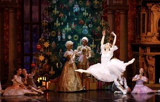 Ballet dancer performing in The Nutcracker in front of a large Christmas tree