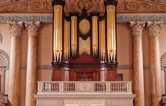 A grand pipe organ located in the Chapel of St Peter & St Paul featuring large golden pipes framed by dark wood and intricate architectural details. T