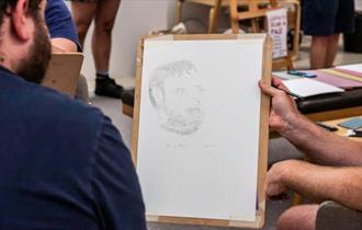 Drawing board being held for neighboring individual to look at with a pencil portrait drawing