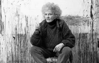 Maggi Hambling seated in front of her artwork