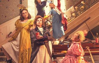 Five women dressed in Regency dresses but modern lace-up boots are having a party. In the foreground, a woman in a yellow satin dress and white pettic