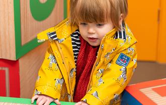 Toddler in yellow jacket playing with a cardboard box