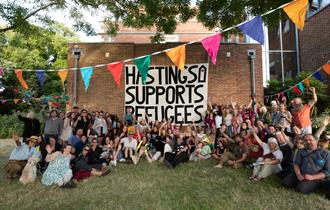 Crowd at Sanctuary Festival surround a large poster that reads 'Hastings supports Refugees'.