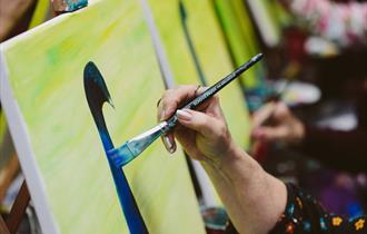 Close up of a canvas in a group setting with a red cup with paintbrushes in it