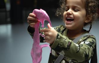 A young girl holding pink slime. The girl is looking at the slime with a big smile on her face.