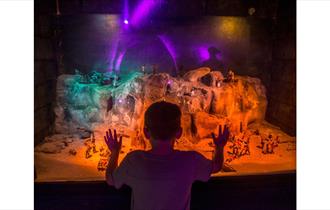 Child looking at a miniature model of smugglers using the caves, at Smugglers adventure Hastings