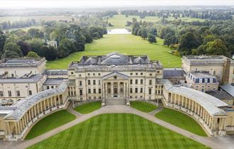 An aerial view of a large golden coloured palace with two wings that curve out either side of the main building held up with Grecian coloumns. The vie
