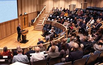 Inside the Fellowship Auditorium at Bletchley Park people are listening to a speaker.