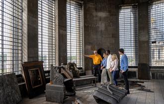 A group of five people, guided by a man in a yellow shirt, are standing inside a large room with tall, grid-patterned windows inside the Chapel Dome a
