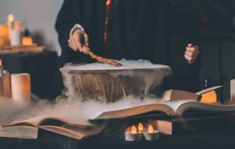 A child preparing a concoction with candles, books and fog in the background