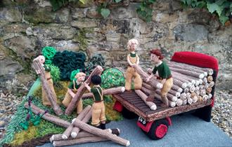 Knitted land girls from WW2 lifting logs.