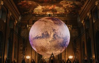 In a grand, ornate hall with a high, frescoed ceilings (the Painted Hall), a large, glowing model of planet Mars is suspended in the centre of the roo