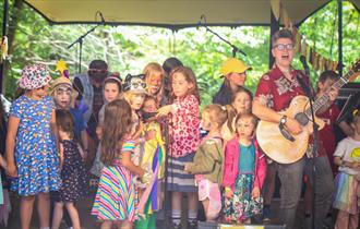 Children on a stage singing with Al Start who is playing the guitar.