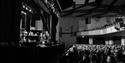 Audience seated inside White Rock Theatre watching live performance on stage in a large auditorium.