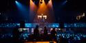 DJ performance at White Rock Theatre with crowd and balcony audience under blue and orange lighting.