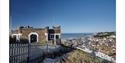 photograph of brick building overlooking town below with sea in the background.