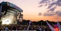 Crowds watching a band on the main stage in the evening with the sun set in the background at the Isle of Wight Festival, music event, what's on