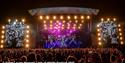 Crowds watching a band on the main stage in the evening at the Isle of Wight Festival, music event, what's on