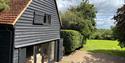 Black cladded barn with wide terrace doors. The view is a green field with trees in the far distance.