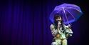 Image courtesy of dfphotography. Image shows a performer on stage in a suit, holding an umbrella