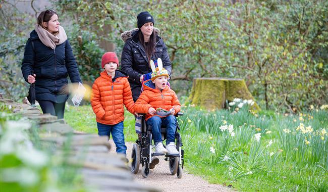Two women walking with two children in orange jackets, one of whom is in a wheelchair, taking part in the Easter trail