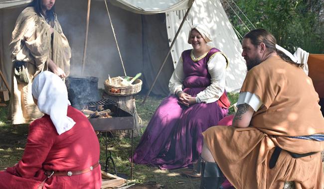People dressed in medieval clothes sat around an open fire