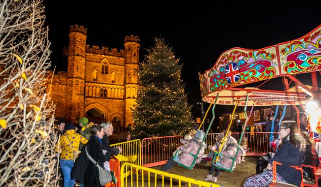 Nightime scene of children's carousel with Battle Abbey illuminated in the background.
