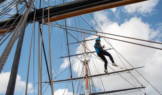A person who is climbing on the rigging of a ship looking back towards the camera