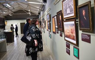 A woman looking at a range of framed photographs inside an exhibition space.