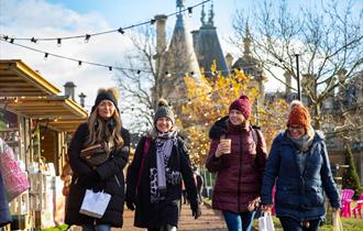 Four women wearing winter clothes walking through a Christmas market